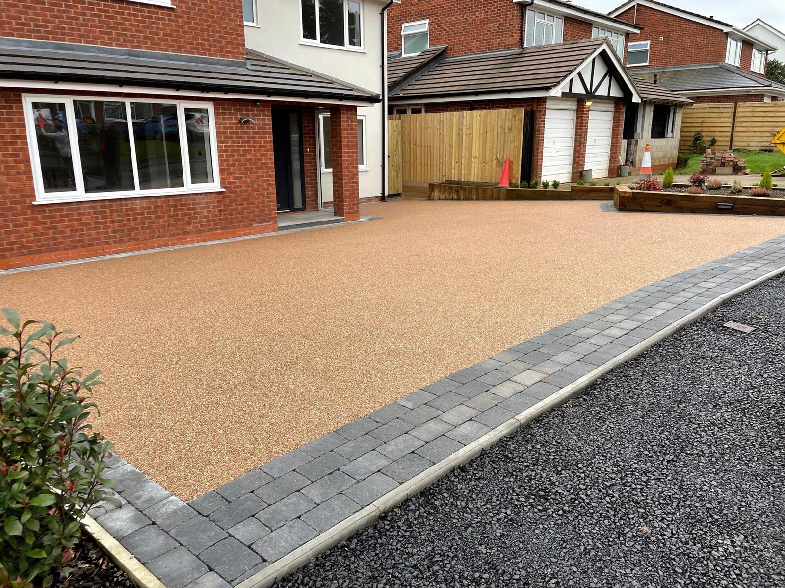 Resin bound driveway with charcoal block paving border in front of a red-brick home